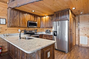 A wooden cabin interior with a kitchen featuring granite countertops, stainless steel appliances, and wooden cabinetry. - Mtn View Fire Pit Hottub Family Pet Friendly (Morganton)