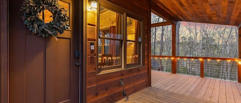 A wooden cabin with a porch, a wreath on the door, and string lights on the railing.