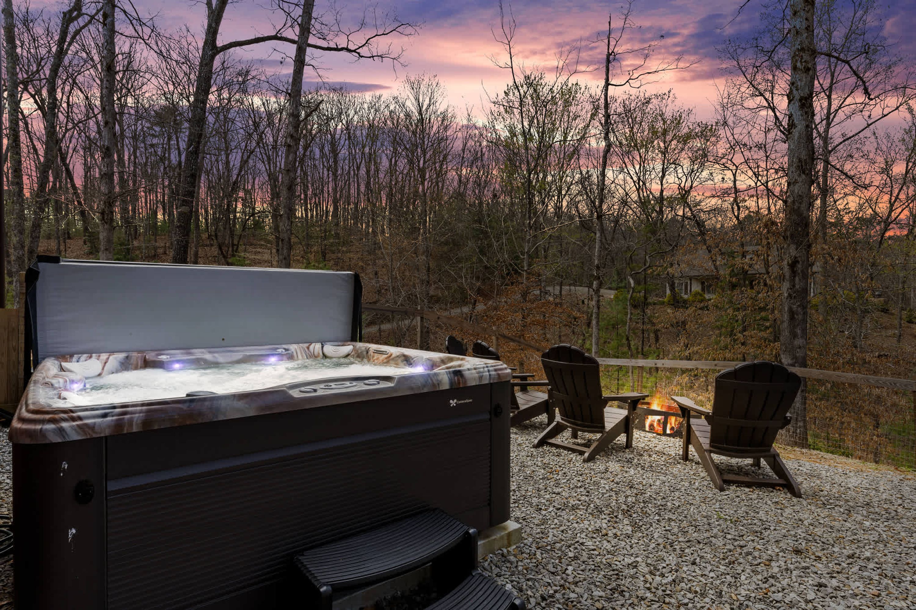 A hot tub with a wooden deck, two Adirondack chairs, and a fire pit.