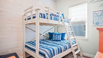 A bunk bed with blue bedding, a ladder, and a window with blinds.