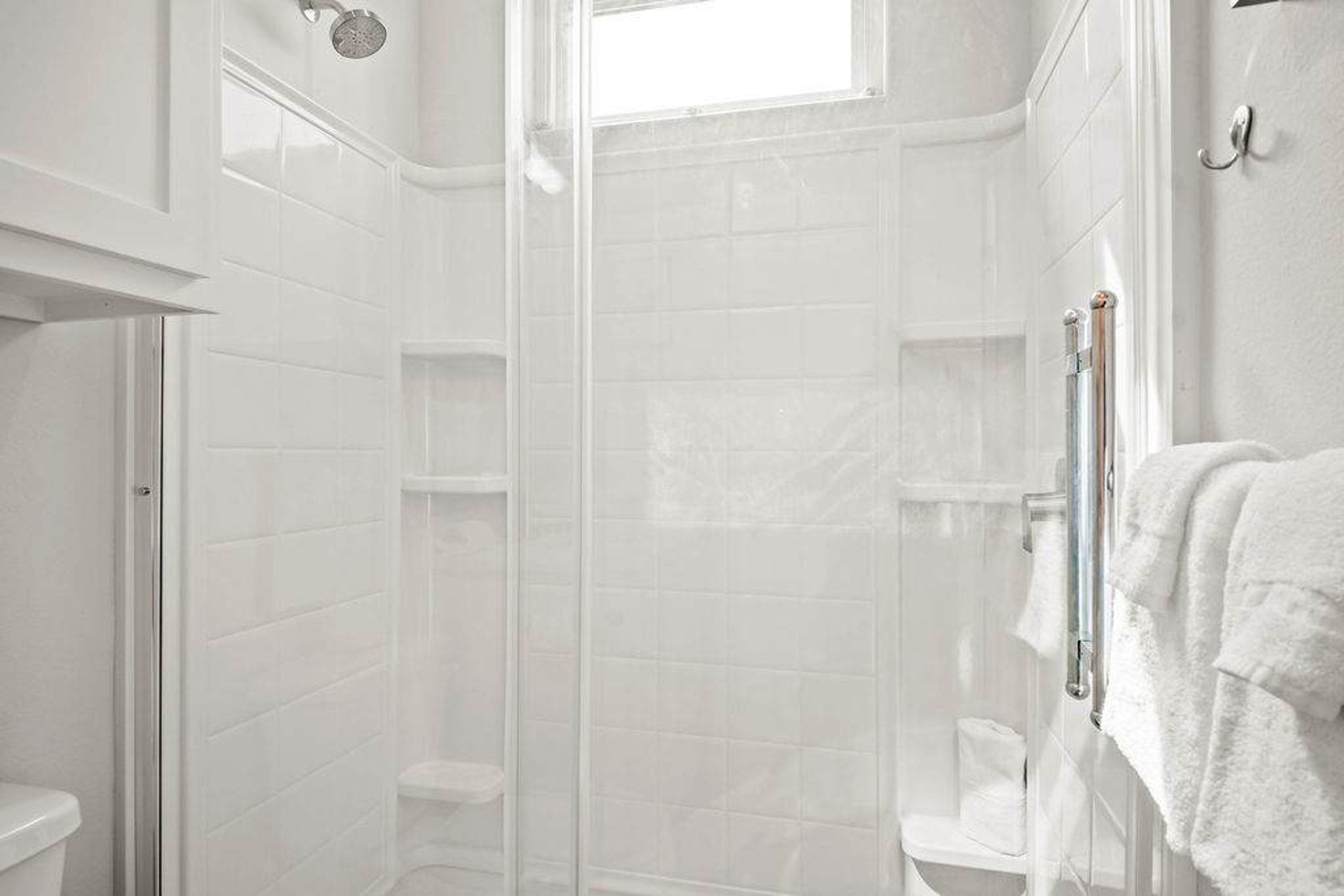 A white tiled shower enclosure with a glass door, a white toilet, and a towel rack.