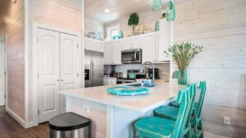 A modern kitchen with white cabinetry, a central island with bar stools, and a stainless steel trash can.