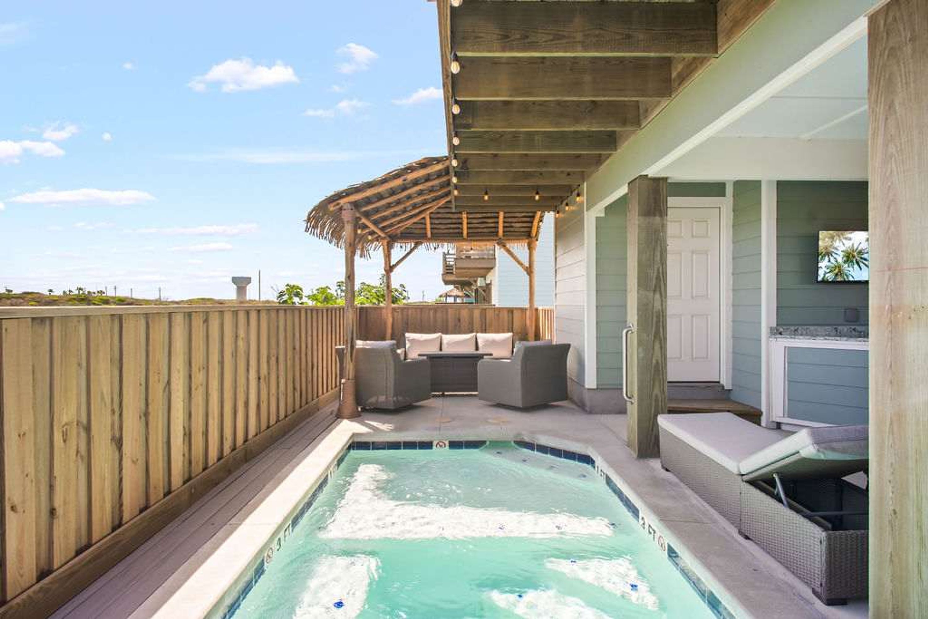 A backyard with a hot tub, outdoor seating, and a covered patio area.