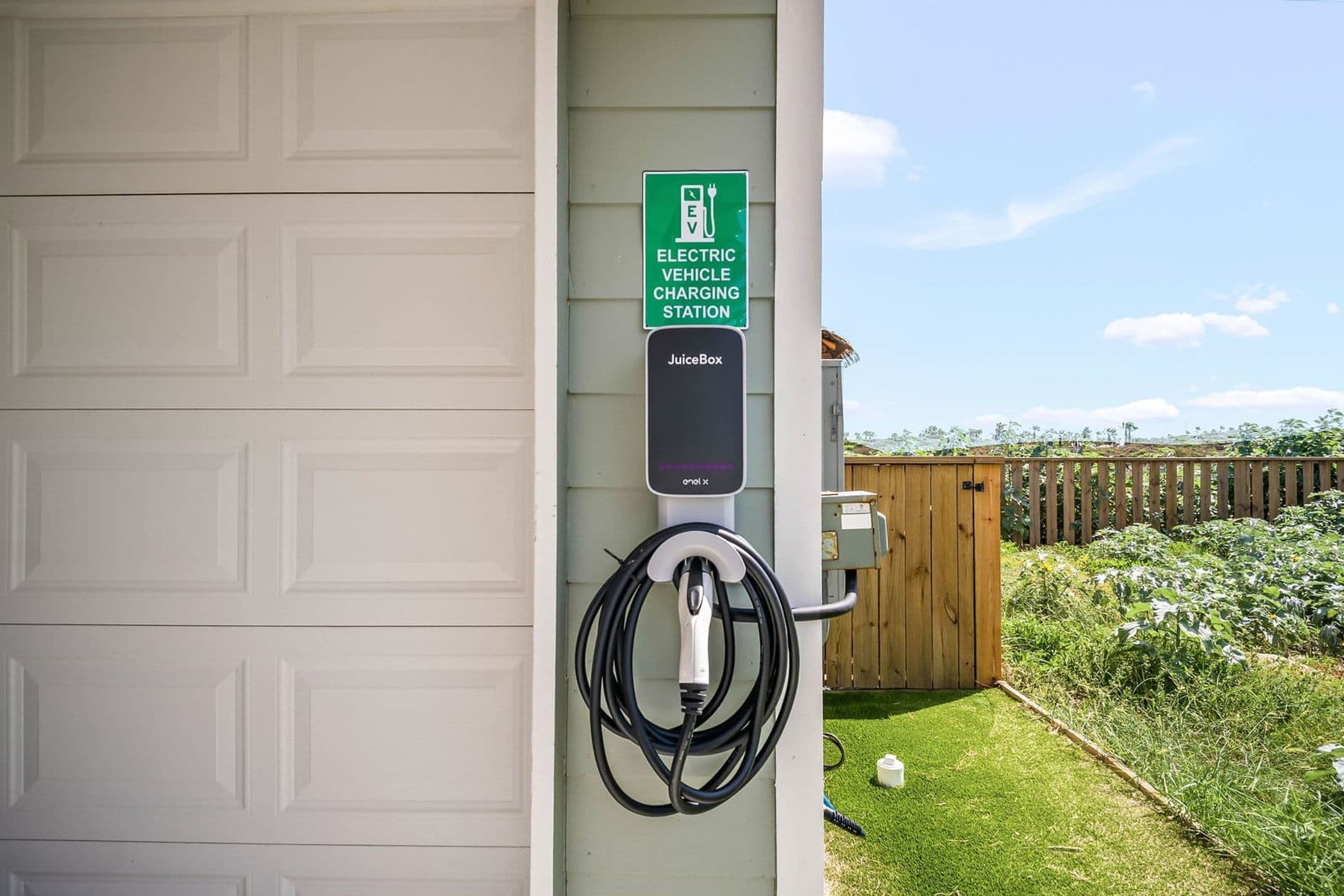 Une borne de recharge pour véhicules électriques fixée à un bâtiment doté d’une porte de garage.