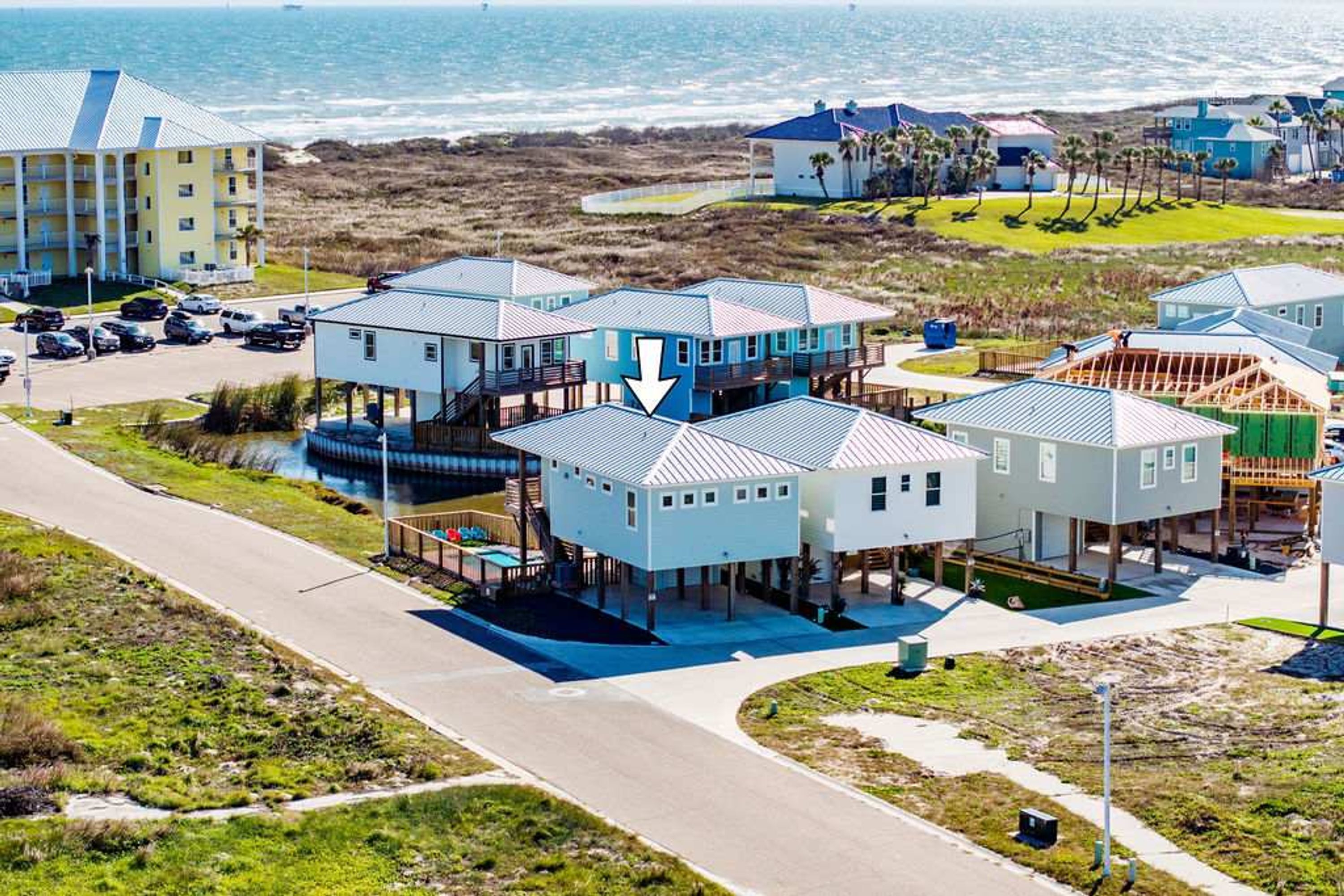 A coastal residential area with multiple houses, a parking lot, and a view of the ocean.