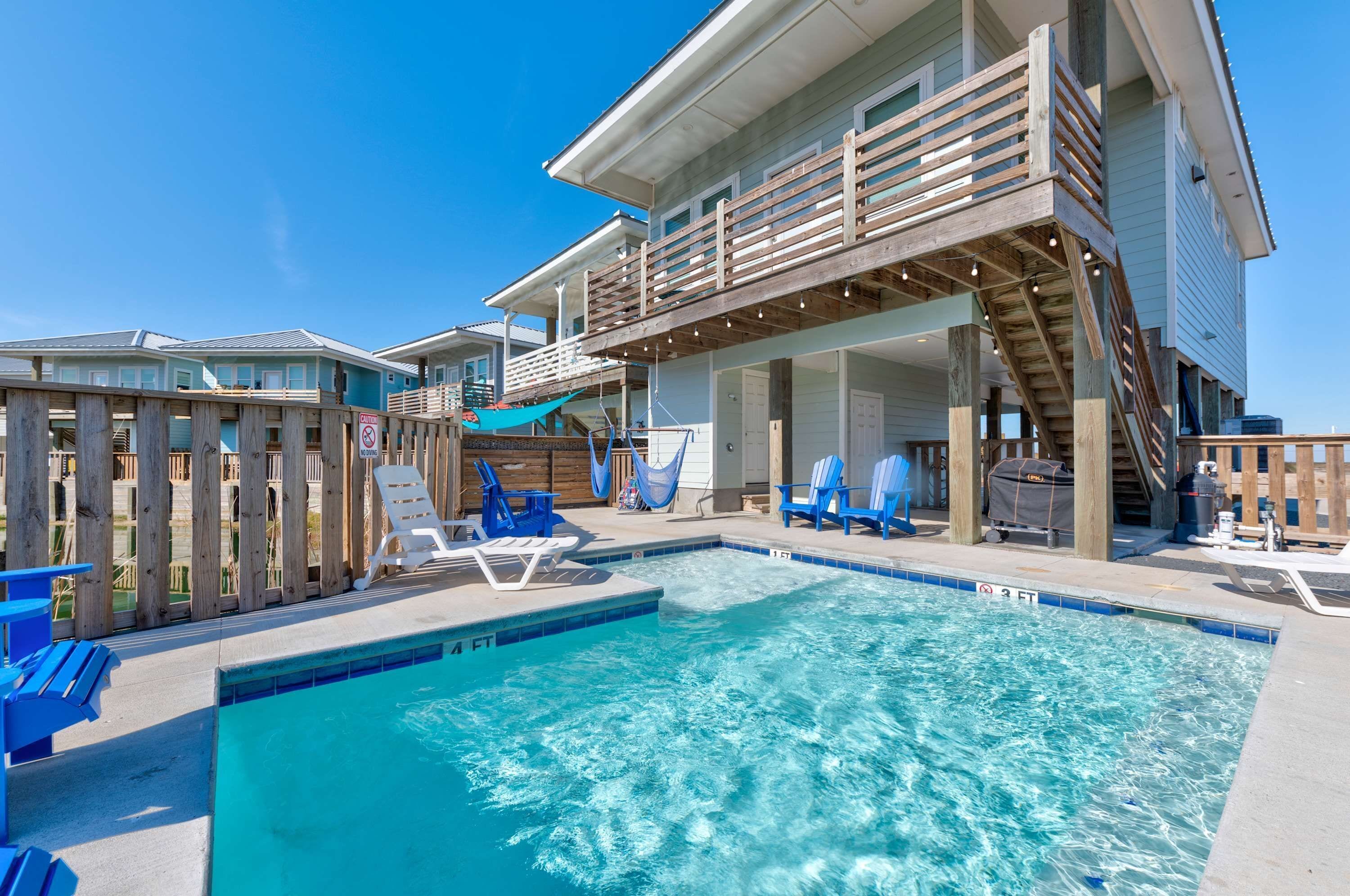A pool area with a wooden deck, lounge chairs, and a building with a balcony.