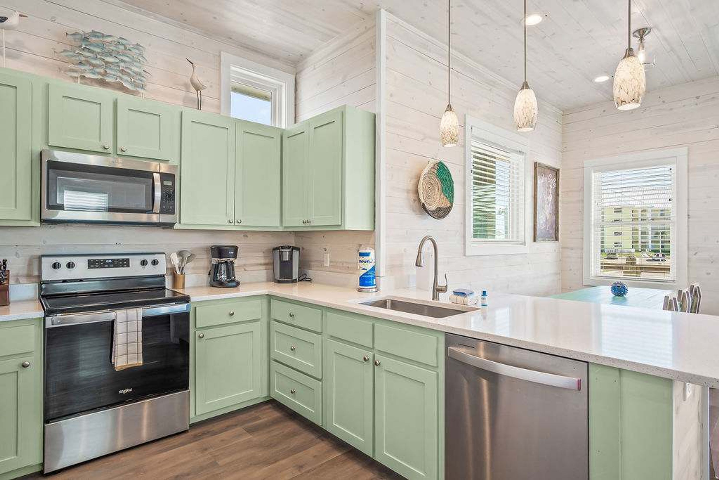 A kitchen with green cabinets, stainless steel appliances, a dishwasher, and pendant lights.