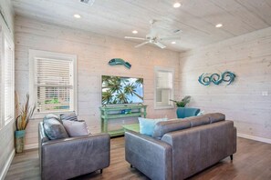 A living room with two sofas, a ceiling fan, and a painting of palm trees. - Save The Ales Boardwalk Private Pool Sleeps 10 (Port Aransas)