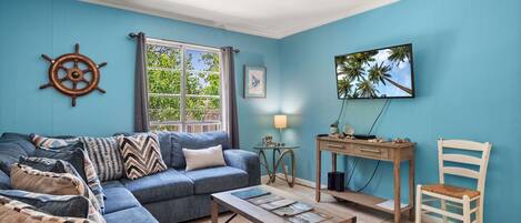A living room with a blue sofa, a wooden coffee table, a desk, and a chair.