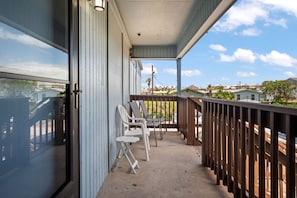 A balcony with a view of a residential area, a wooden railing, and two white chairs. - The Codfather- Family Friendly 2 Minute to Beach (Port Aransas)