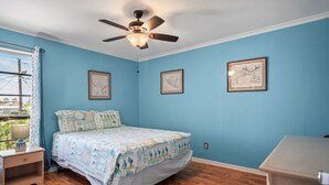 Un dormitorio con cama, mesita de noche, ventilador de techo y cuadros en la pared.