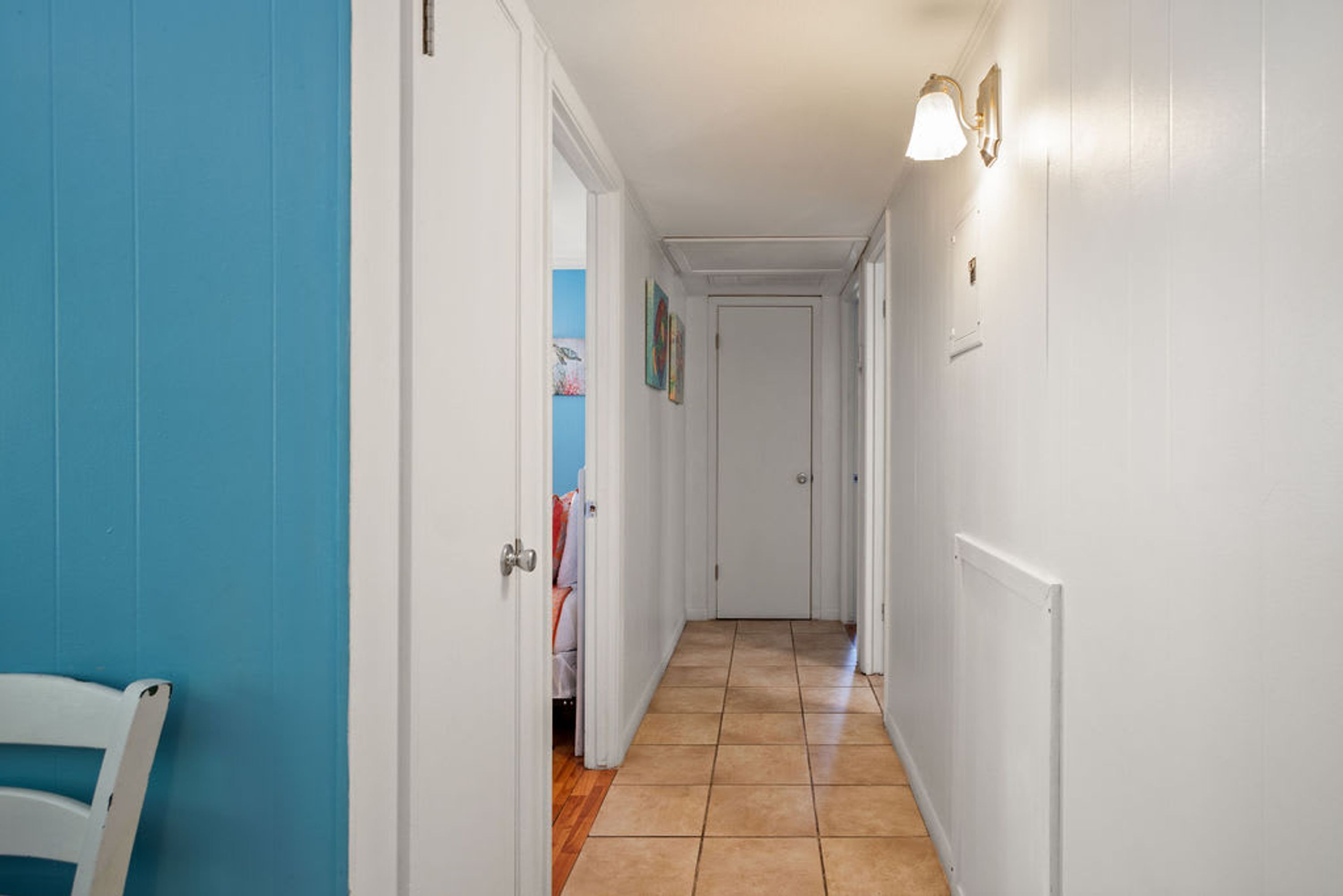 A hallway with white walls, a blue door, and a tiled floor.
