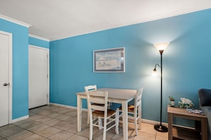A room with a blue wall, a white door, a dining table with chairs, a floor lamp, and a framed picture on the wall. - The Codfather- Family Friendly 2 Minute to Beach (Port Aransas)