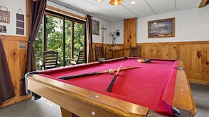 A pool table with a red felt surface, wooden surroundings, and a view of greenery outside. - Mountain Views-hot Tub-games-pool Foosball (Morganton)