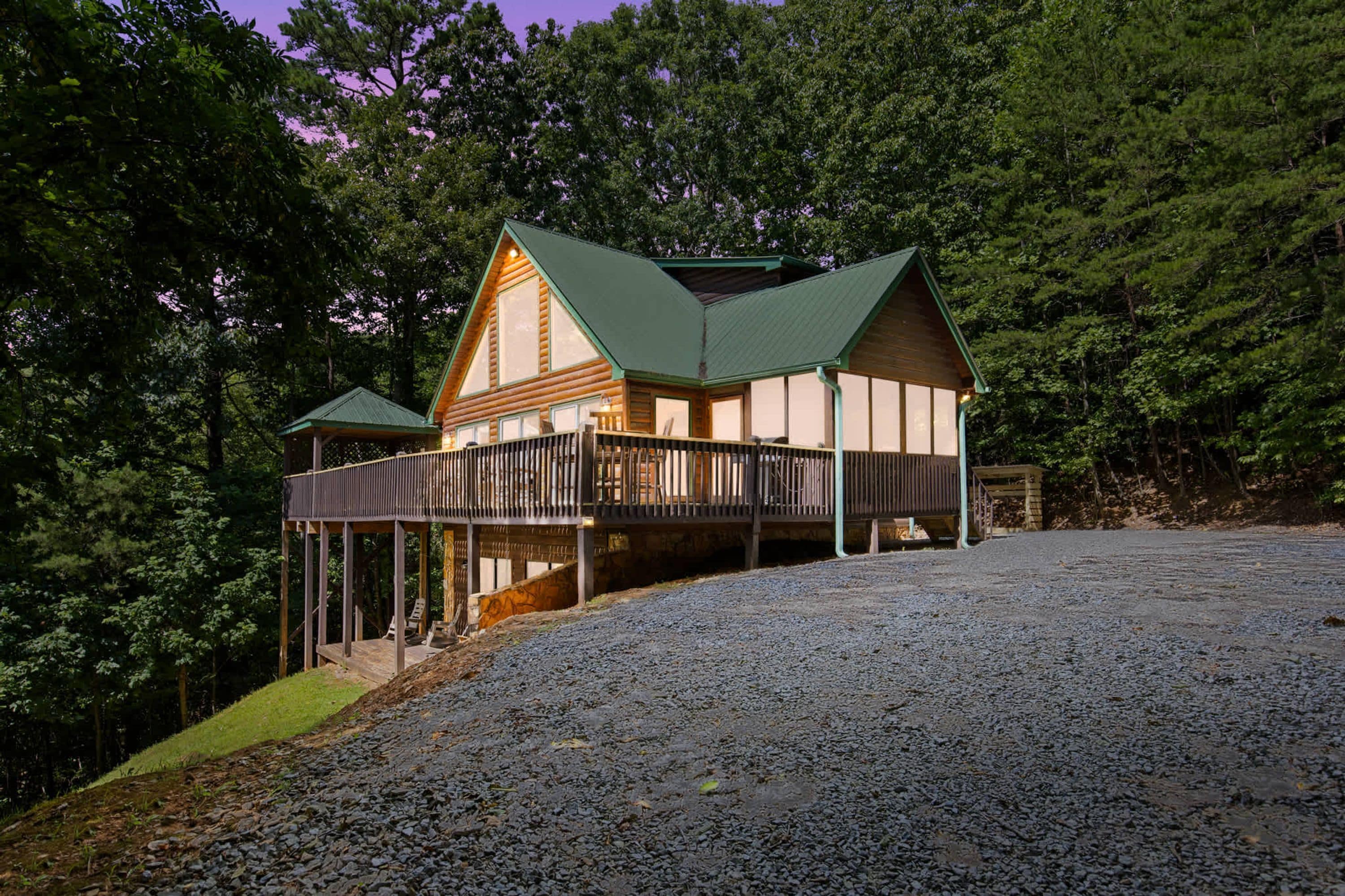 A two-story log cabin with a covered porch and a gravel driveway.