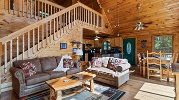 L’intérieur d’un chalet en bois comprend un escalier, deux canapés, une table basse, une table à manger et un coin cuisine.