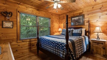 Un dormitorio tipo cabaña de madera con cama con dosel, ventilador de techo y una ventana grande con persianas.