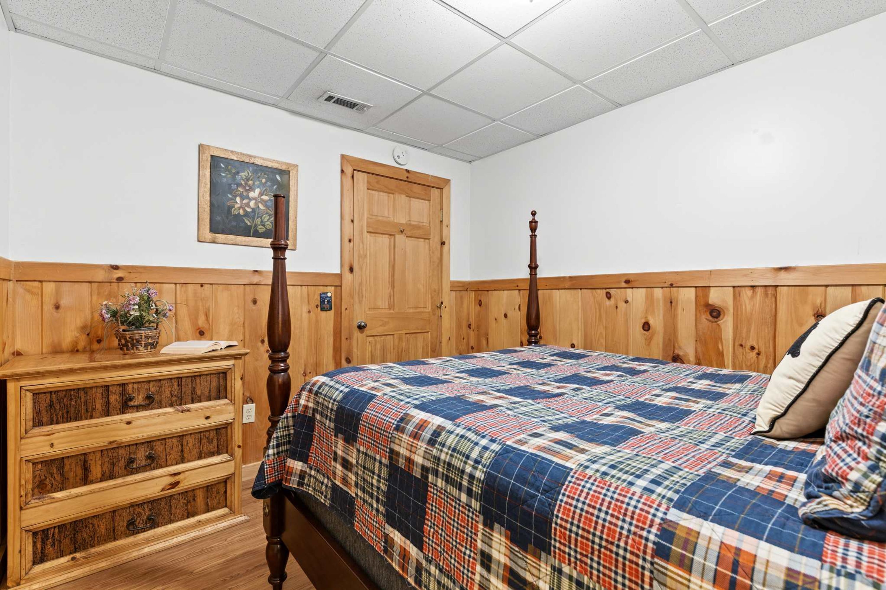 Quarto com cabeceira de madeira, colcha acolchoada, cômoda de madeira e uma porta.
