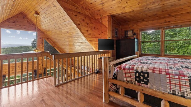 A cabin with a wooden interior, a bed with a quilt, a television, and a balcony with a railing. - Mountain Views-hot Tub-games-pool Foosball (Morganton)