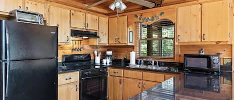A kitchen with wooden cabinets, a black refrigerator, a stove, a microwave, and a ceiling fan.