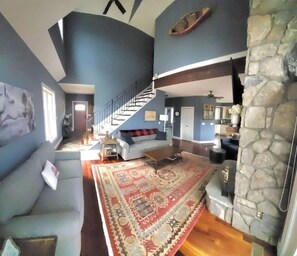 A spacious living area with a large rug, a staircase, and a stone fireplace. - Lakefront Dock Hot tub Firepit Dog Friendly (Mill Spring)