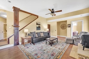 A living room with a staircase, a ceiling fan, a sofa, a coffee table, and a rug. - Lakefront Dock Hot tub Firepit Dog Friendly (Mill Spring)