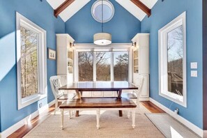 A dining room with a large table, white chairs, and a view through the windows. - Lakefront Dock Hot tub Firepit Dog Friendly (Mill Spring)