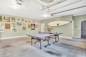 A room with a ping pong table, a surfboard, and various posters on the walls. - Lakefront Dock Hot tub Firepit Dog Friendly (Mill Spring)