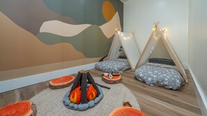 Una habitación acogedora con un mural, dos tiendas tipi, un hogar a leña y cojines con estampado de estrellas.