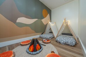 Una habitación acogedora con un mural, dos tiendas tipi, un hogar a leña y cojines con estampado de estrellas.