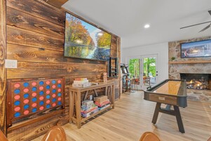 A room with a pool table, a GoSports game, a television mounted on a wooden wall, and a fireplace.
