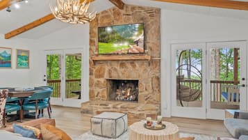 A spacious living room with a stone fireplace, a television mounted on the wall, and a dining area with a table and chairs.