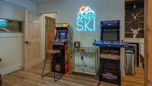Una habitación con suelo de madera, juegos de arcade, un letrero de neón y una zona de bar con estanterías.