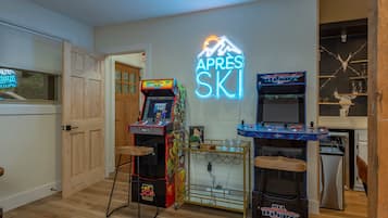 A room with wooden flooring, arcade games, a neon sign, and a bar area with shelves.