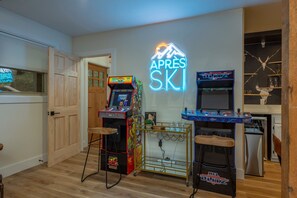 Una habitación con suelo de madera, juegos de arcade, un letrero de neón y una zona de bar con estanterías.