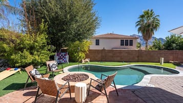 A backyard with a swimming pool, outdoor furniture, and a house in the background.
