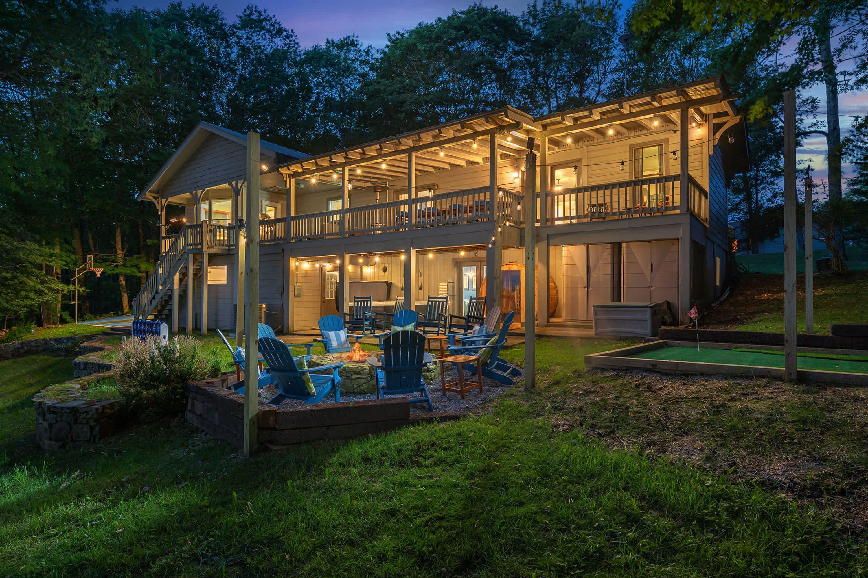 A two-story wooden house with a covered porch, outdoor seating area, and a small putting green.