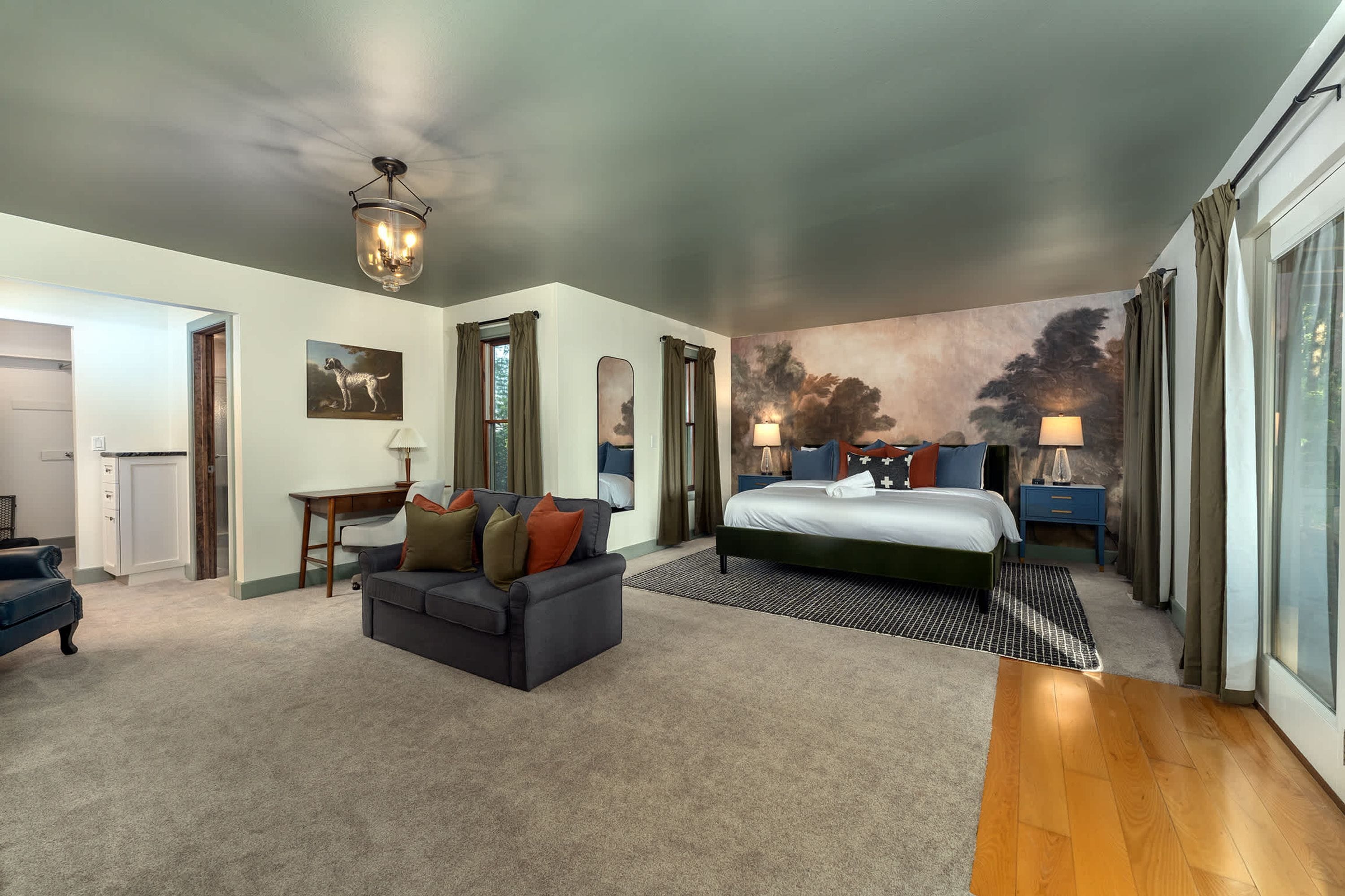 A hotel room with a bed, a sofa, a desk, and a large painting on the wall.