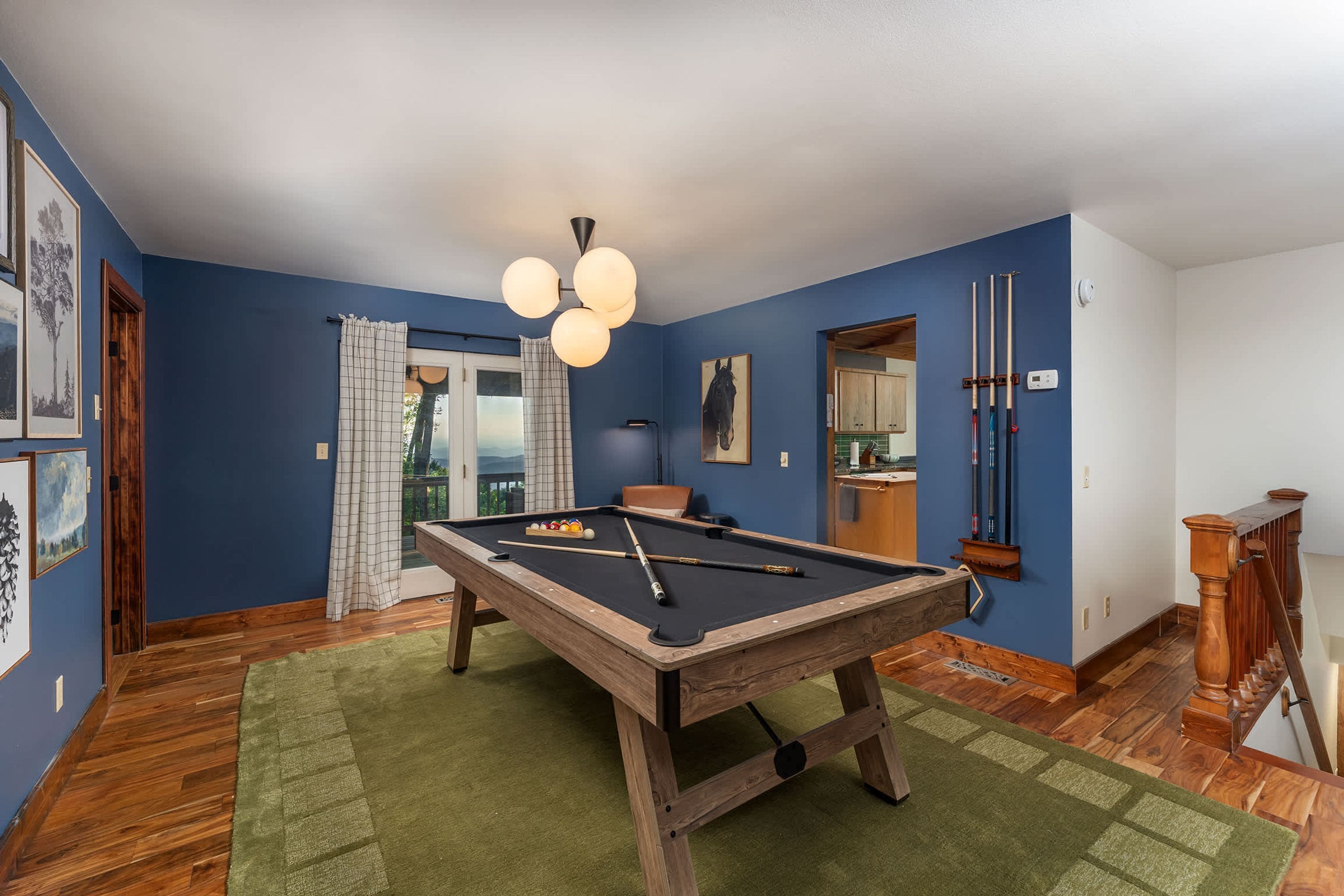 A pool table in a room with blue walls, a wooden floor, and a green rug.