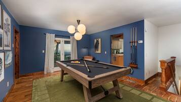 A pool table in a room with blue walls, a wooden floor, and a green rug.