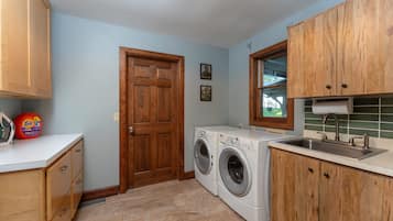 A laundry room with a washing machine, a sink, wooden cabinets, and a door.