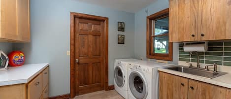 Una lavandería con lavadora, lavadero, armarios de madera y una puerta.