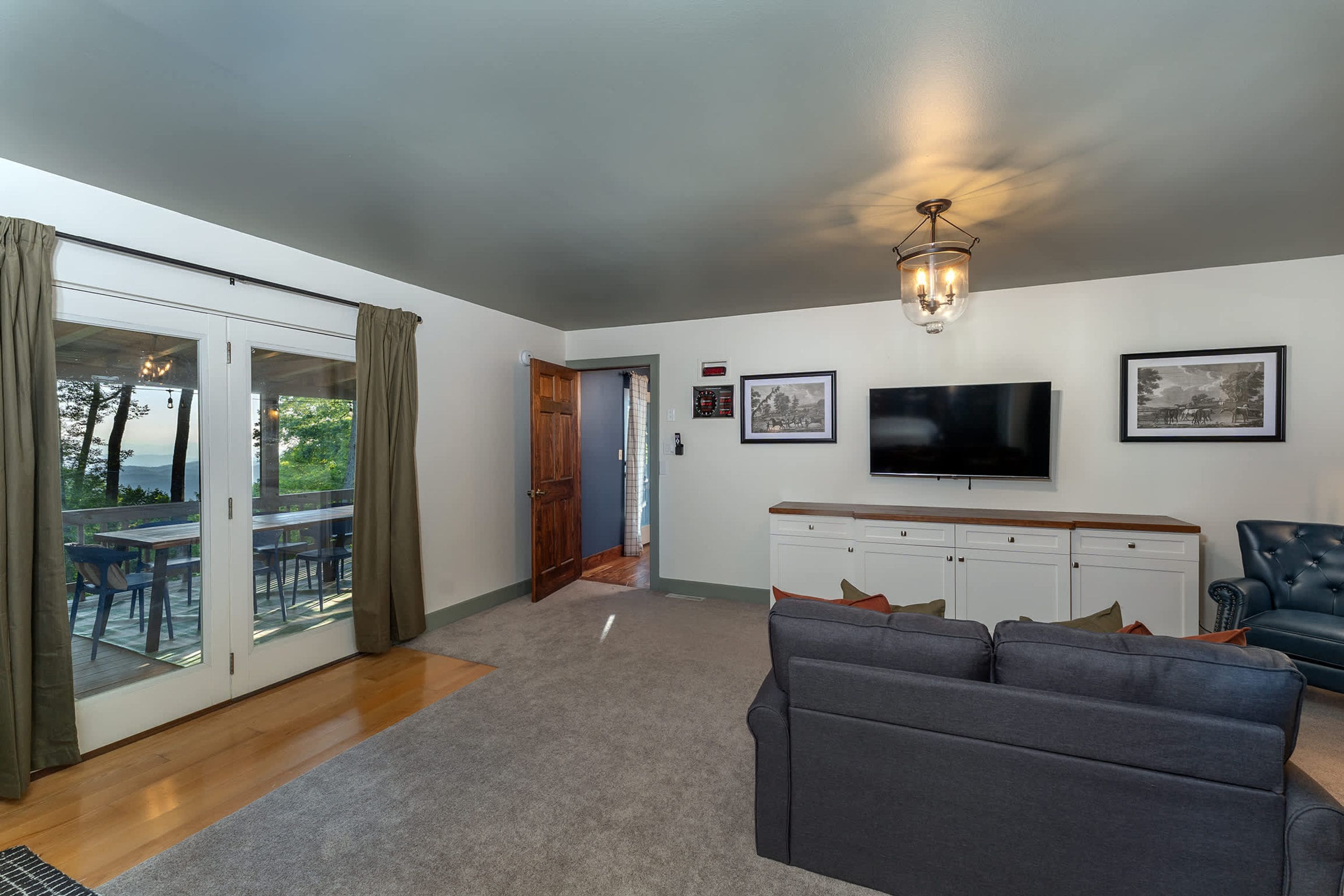 A living room with a grey sofa, a flat-screen TV, and a chandelier.