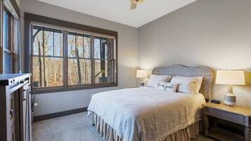 A bedroom with a bed, a nightstand, a lamp, a clock, and a window with a view of trees.