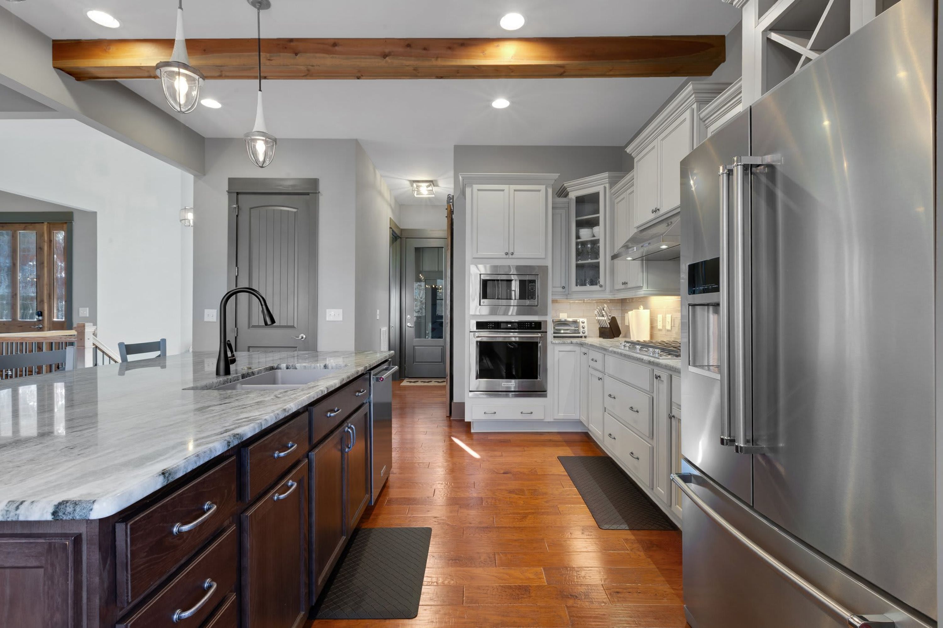 A modern kitchen with stainless steel appliances, wooden flooring, and a marble countertop.