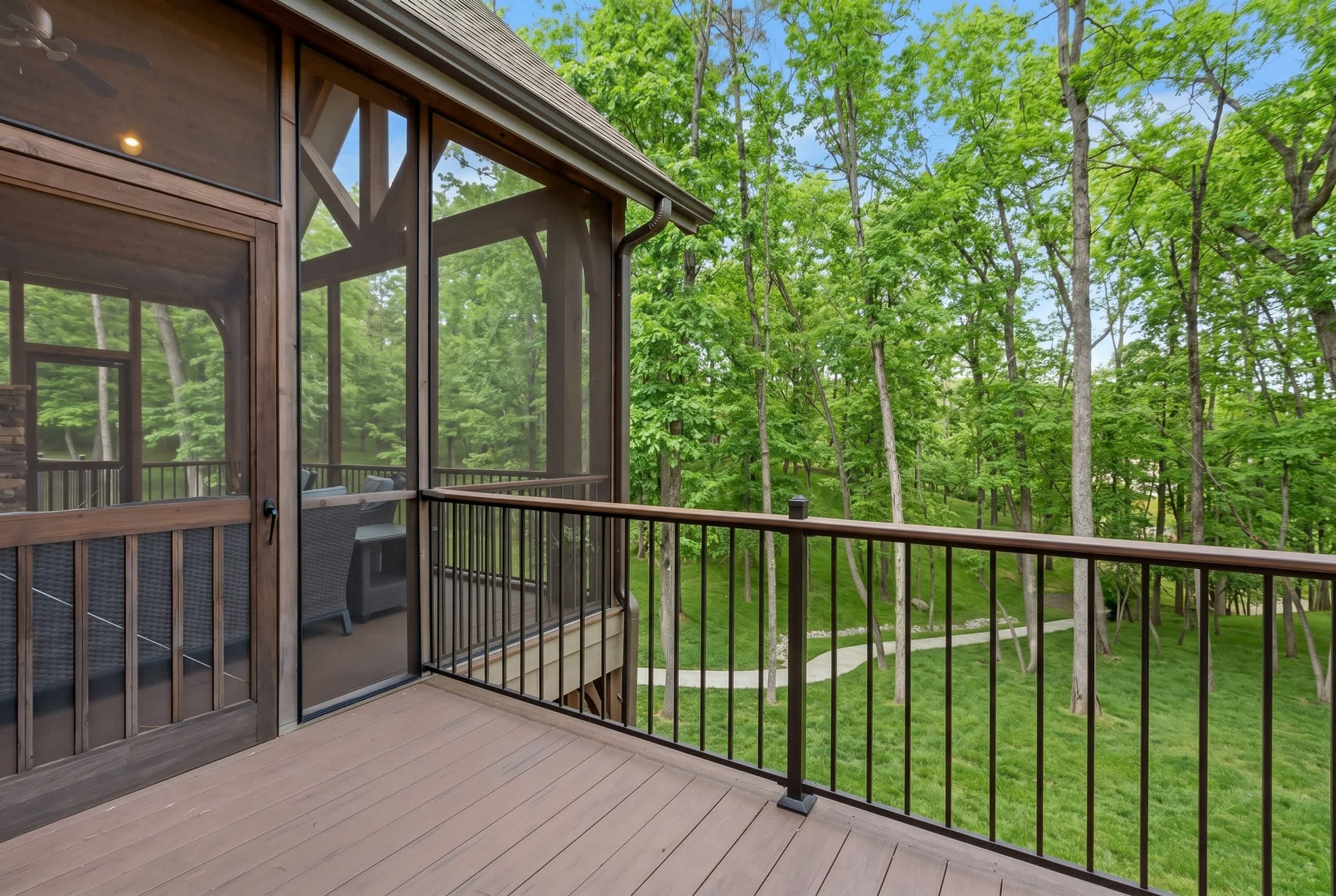 A wooden deck with a glass door leading to an outdoor seating area, surrounded by a metal railing and a view of a wooded area.