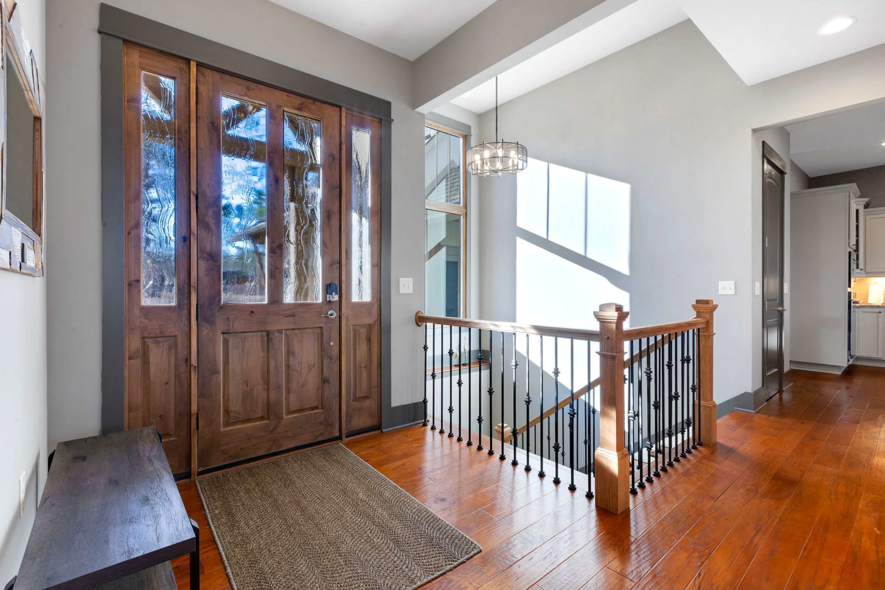 A wooden staircase with a metal railing, a wooden bench, and a rug leading to a door with frosted glass panels.