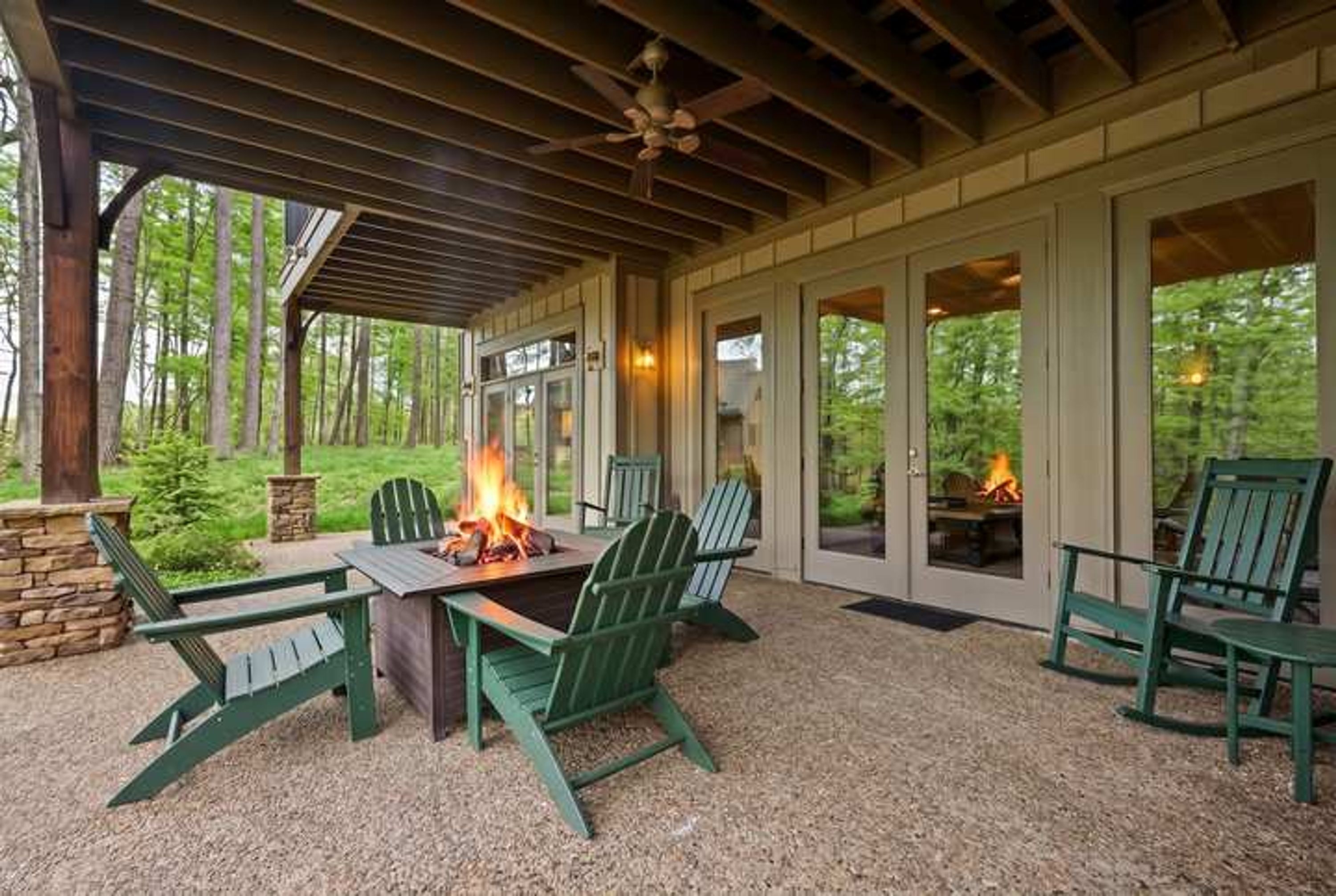 Eine Terrasse im Freien mit Feuerstelle, grünen Adirondack-Stühlen und einer Steinmauer.