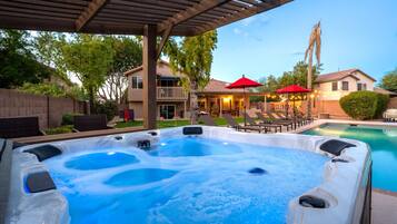 Un espace avec un jacuzzi, une piscine, des sièges extérieurs et un patio couvert.