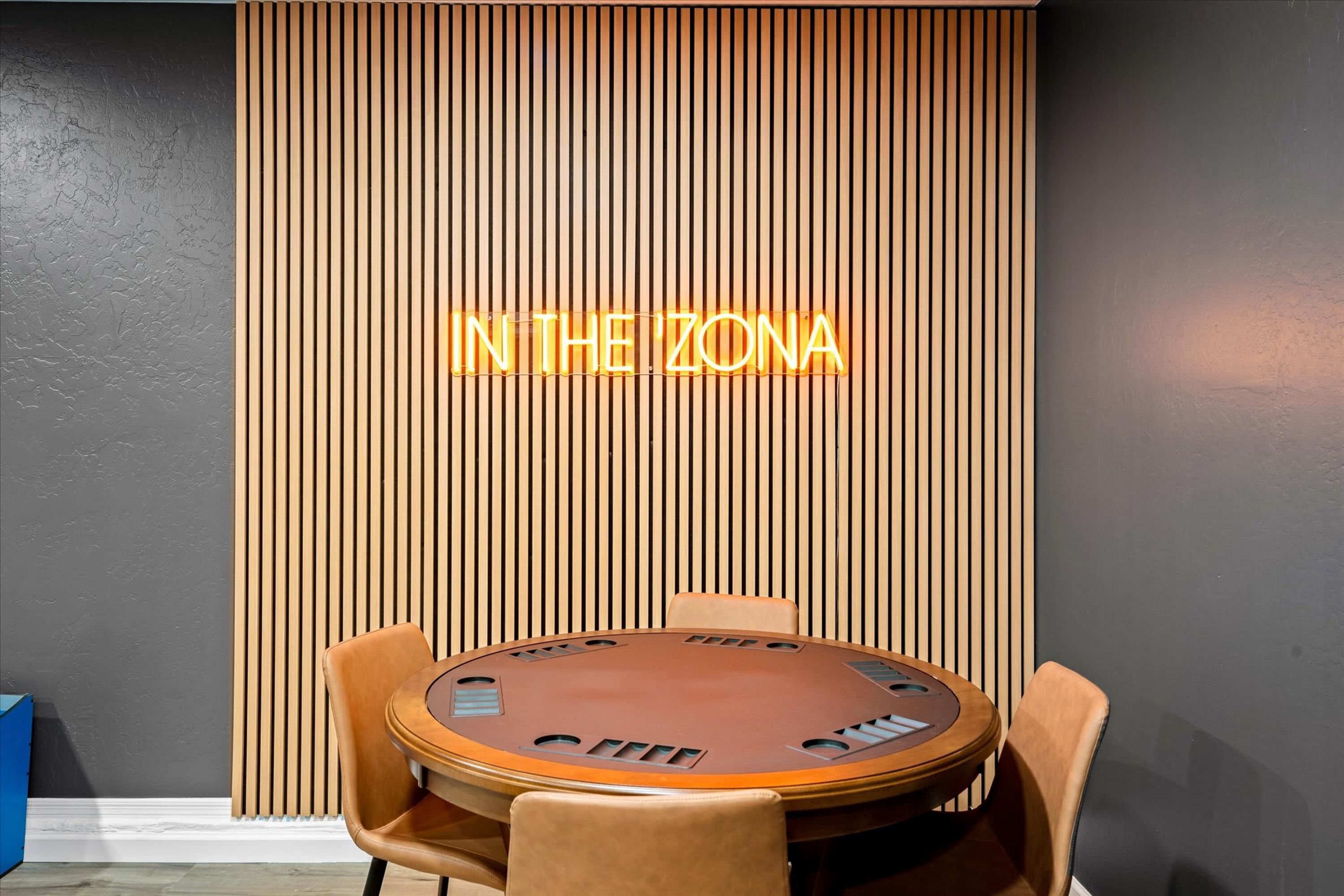 A room with a wooden slat wall and a neon sign that reads 'IN THE ZONA'.